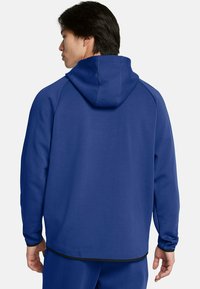 Sudadera con capucha en un azul vibrante, con una tela suave y texturizada. Presenta mangas raglán y un dobladillo negro en la parte inferior.