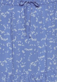 Tissu bleu avec petit imprimé floral blanc, taille froncée avec cordon à nouer et détail volanté sur l'ourlet.