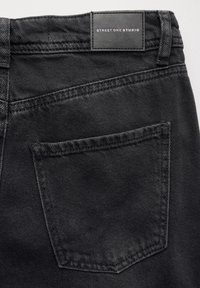 Vaqueros de mezclilla negra con un bolsillo trasero y una etiqueta de la marca cosida en la cintura, con una textura suave y un ajuste estándar.