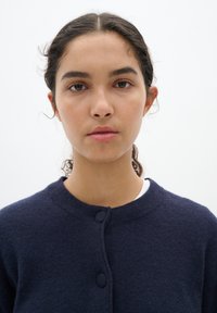 Mörkblå ullcardigan med rund halsringning, prydd med två stora knappar framtill och ett strukturerat stickmönster.