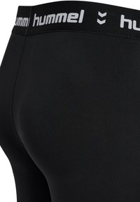 Czarne legginsy o gładkiej fakturze z szerokim czarnym pasem w talii z białym logo "hummel". Zbliżenie na tył.