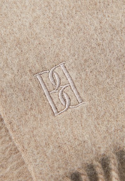Écharpe en laine beige avec une texture douce, ornée d'un monogramme brodé dans un fil assorti et discret à une extrémité.