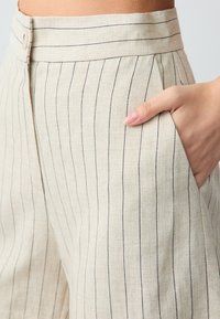 Beige linnen broek met een rechte snit, voorzien van verticale zwarte strepen, een platte tailleband en zijzakken. Gladde textuur.