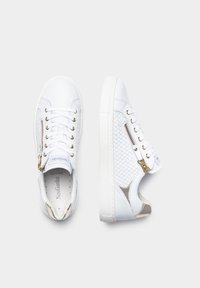 Zapatillas blancas con textura trenzada, ojales dorados, cremalleras laterales y una suela lisa. Los acentos incluyen un inserto brillante en el lateral.
