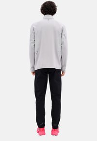 Light gray long-sleeve jacket with mesh side panels, paired with black pants and bright pink athletic shoes, shown from the back.