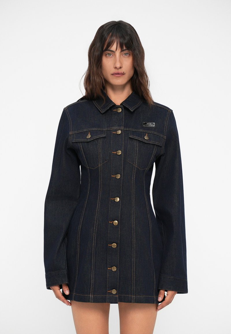 Σκούρο μπλε τζιν φόρεμα με μακριά μανίκια, μπροστινούς κουμπιά και δύο τσέπες στο στήθος. Διαθέτει αντίθετο ράψιμο και σχέδιο σε στενή γραμμή.