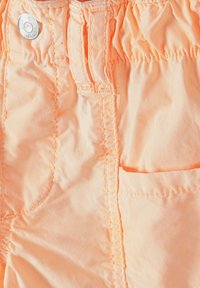 Pfirsichfarbene Stoffshorts mit elastischem Bund, mit Steppdetails und einer Seitentasche. Glatte Oberfläche und leichtes Material.