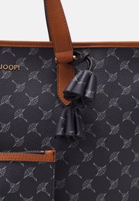 Tote-laukku, jossa on laivastonsininen teksturoitu synteettinen materiaali ja hopeanvärinen kuvio abstrakteista muodoista. Sisältää ruskeat nahkaosat ja tupsukoristeen.