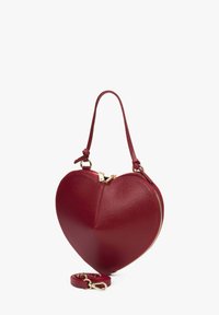 Rode leren handtas in hartvorm met gouden ritssluiting, korte handvat die aan de uiteinden is omgevouwen, en afneembare lange schouderriem op een witte achtergrond.