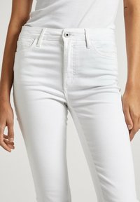 Vita denimjeans med en åtsittande design, hög midja och femficksstil. Har en framknäppning och subtil textur.