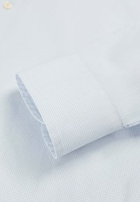 Poignet de chemise à carreaux bleu clair, présentant des carreaux subtils, un tissu doux et une finition soignée. Détails visibles des boutons et des coutures.