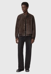 Brązowa skórzana kurtka bombowiec z zapięciem na guziki i ściśle przylegającymi mankietami, zestawiona z prostymi czarnymi dżinsami i czarnymi butami.