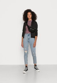 Casaco bomber preto, top texturizado em bordô, jeans claros rasgados e ténis altos pretos. Bolsa transversal preta com detalhes em prata.