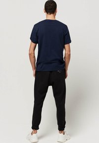 Marineblauwe katoenen T-shirt met een ronde hals, gecombineerd met zwarte tapered joggers. De joggers hebben opgerolde boorden en zijn gemaakt van zachte stof. Witte sneakers zijn zichtbaar.