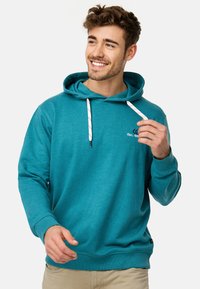 Teal hoodie med kængurulomme, snoretræk i hætten og ribbet manchetter. Har et hvidt broderet logo på brystet. Blødt stof.