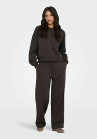 Mørkebrun sweatshirt med afslappet pasform og ribbet manchetter, parret med matchende løstsiddende sweatpants og bløde fodtøj.