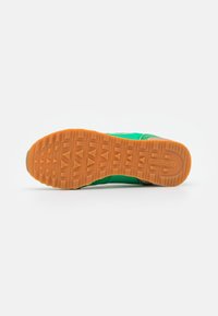Zapatillas verdes con suela de goma texturizada en naranja, que presentan un diseño estilizado y materiales contrastantes en la parte superior.