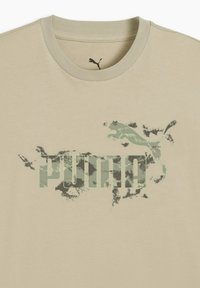 T-shirt en coton beige avec un grand logo "PUMA" en camouflage vert et un graphisme de puma en plein saut, col rond et manches courtes.