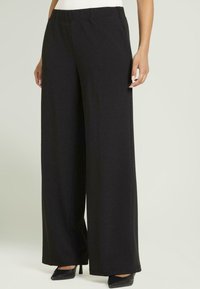 Pantalones negros de pierna ancha hechos de una tela suave y texturizada. La cintura es elástica y el diseño presenta una silueta limpia y minimalista.