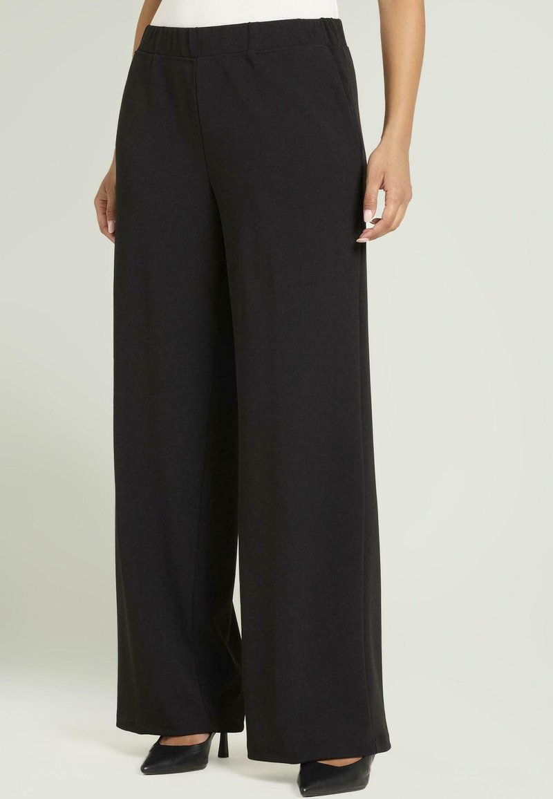 Pantalones negros de pierna ancha hechos de una tela suave y texturizada. La cintura es elástica y el diseño presenta una silueta limpia y minimalista.