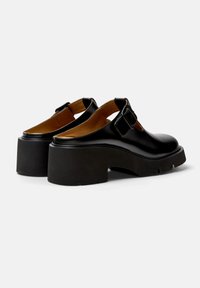 Pantofi slingback din piele neagră, cu o talpă platformă robustă și detalii cu cataramă, având o textură fină și un design cu vârful rotunjit.