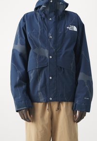 Voděodolná námořnicky modrá bunda s mramorovým vzorem, předními zapínáními na druky a nastavitelnými manžetami. Obsahuje kapuci a značkové detaily.