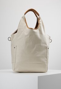 Beige struktureret tote taske med lysebrune polstrede håndtag, sidelommer med trykknapper og metalringe på begge sider.