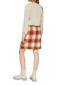 Sweatshirt in hellem Beige, strukturierter Stoff, kombiniert mit einem karierten Rock in Braun und Creme. Weiße Knöchelstiefel mit einer klobigen Sohle.