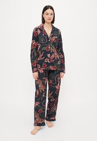 O conjunto de pijama floral azul marinho apresenta uma camisa com botões e calças combinando, decorado com padrões de leopardos e folhas tropicais em cores vibrantes.