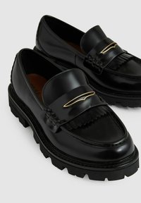 Sorte læder loafers med en glat finish, prydet med en frynset rem og hardware i guldtoner. Kraftig gummisål med tekstureret detaljering.