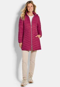 Fuchsia gewatteerde jas met een capuchon, ritsluiting en chevronpatroon; gecombineerd met beige broek en lichte sneakers.