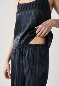 Set da notte in satin scuro con righe verticali, spalline sottili e cintura elastica. Texture liscia con una leggera lucentezza e dettaglio con taglio laterale.