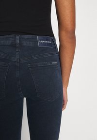 Mörkblå denimjeans med hög midja. Funktioner inkluderar bakfickor, subtila sömnadsdetaljer och en Calvin Klein-etikett på midjebandet.