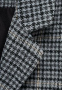 Gray plaid wool fabric with a soft texture, featuring a houndstooth pattern in black and beige tones, folded at the corner.
