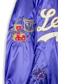 Giacca di raso viola con toppe ricamate, tra cui un logo, stelle e il testo "GRMY" in accenti bianchi e dorati.