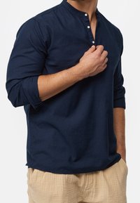 Camicia a maniche lunghe blu navy in morbido cotone, con scollo alla henley con tre bottoni frontali e maniche arrotolate.