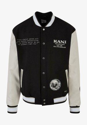 Mustaa ja kermaista väritystä oleva yliopistotakki, jossa on erottuvat hihat, brodeerattu logo, napsulukot, raidalliset ribbikuvioidut hihansuut ja painettu teksti vasemmalla puolella.