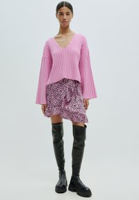Rosa gerippter Pullover mit tiefem V-Ausschnitt, kombiniert mit einem rosa und schwarzen Leopardenmuster-Rüschensrock und knielangen schwarzen Plateaustiefeln.