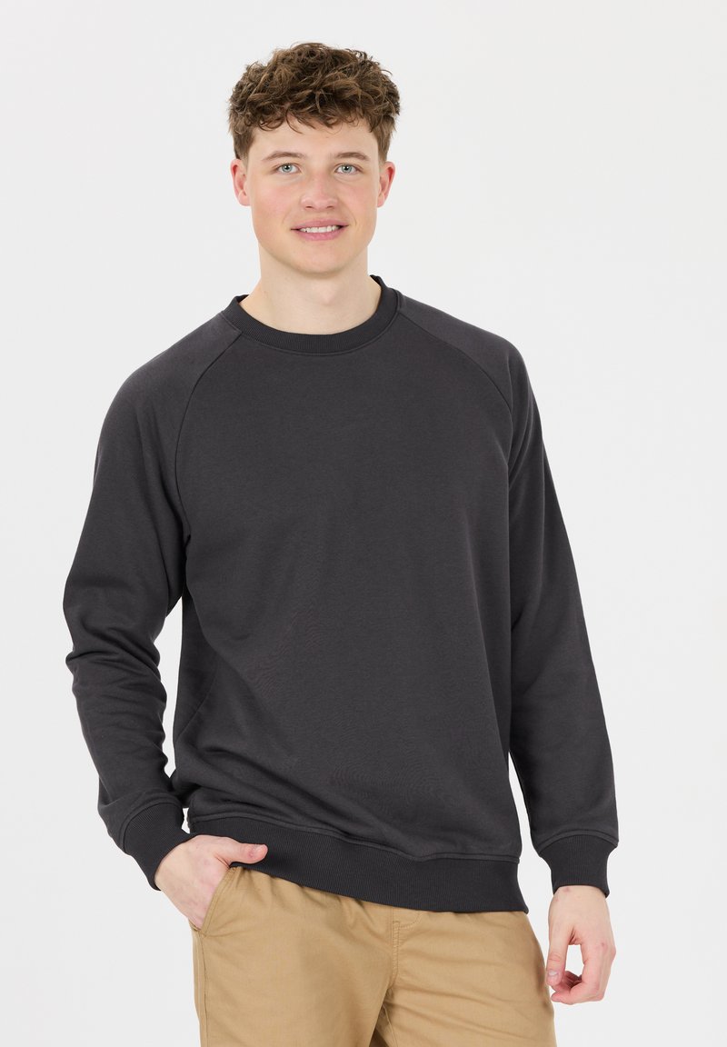 Sweatshirt gris foncé avec des manches longues, un col rond, des poignets et un ourlet côtelés, fabriqué dans un tissu doux. Porté avec un pantalon beige clair.