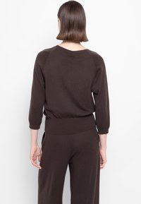 Maglione a maglia marrone scuro con collo a giro, maniche raglan a tre quarti e orlo a costine. Texture liscia con vestibilità comoda.