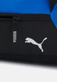Sac à dos de sport noir et bleu avec une texture lisse, un compartiment zippé et un logo Puma blanc bien en vue.
