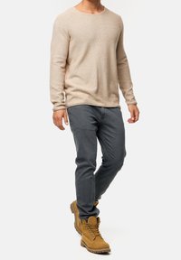 Beiges, langärmeliges Strickshirt kombiniert mit grauen Jeans aus Denim und braunen Schnürstiefeln. Das Shirt verfügt über einen Rundhalsausschnitt und eine strukturierte Stoffqualität.