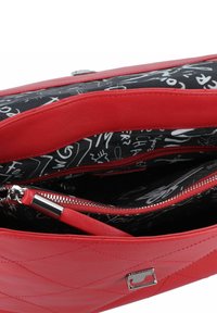Bolso de mano de cuero rojo con un diseño acolchado, que presenta un interior negro forrado con patrones abstractos en blanco. Incluye compartimentos con cremalleras.