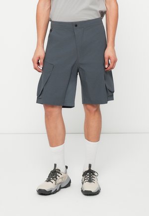 Graue Cargo-Shorts aus leichtem Material, mit Seitentaschen, einer taillierten Taille und einem geraden Saum. Getragen mit beigen Sneakern.