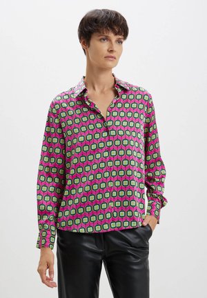 Chemise boutonnée avec un imprimé géométrique vibrant, présentant des carrés verts, roses et noirs sur un fond rose, avec des manches longues et un col.