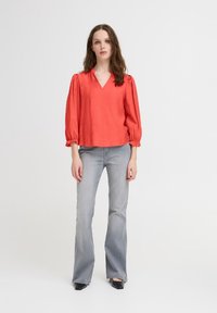 Koralo palaidinė su V formos iškirpte ir pūstomis rankovėmis, derinama su šviesiai pilkais platėjančiais džinsais ir juodais bateliais su smailiu nosimi. Paprastas dizainas, tekstūruota medžiaga.