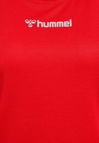 Czerwona koszulka sportowa z teksturowanym wykończeniem; na górnej lewej stronie znajduje się jasnoszare logo "hummel". Casualowy, dopasowany krój.