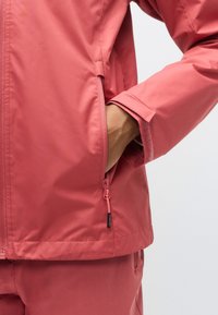 Vanntett rosa jakke med glatt tekstur, glidelåslomme på siden og ribbede mansjetter, med rett kant for en avslappet passform.