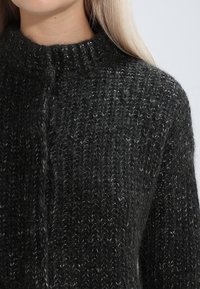 Knit sweater in dark gray with a chunky texture, featuring a high neck and subtle horizontal ribbing detail. Front button closure.
