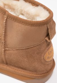 Stivale alla caviglia in suede marrone con una morbida fodera in pile bianco. Presenta dettagli cuciti e una patch in pelle con il marchio sul lato esterno.